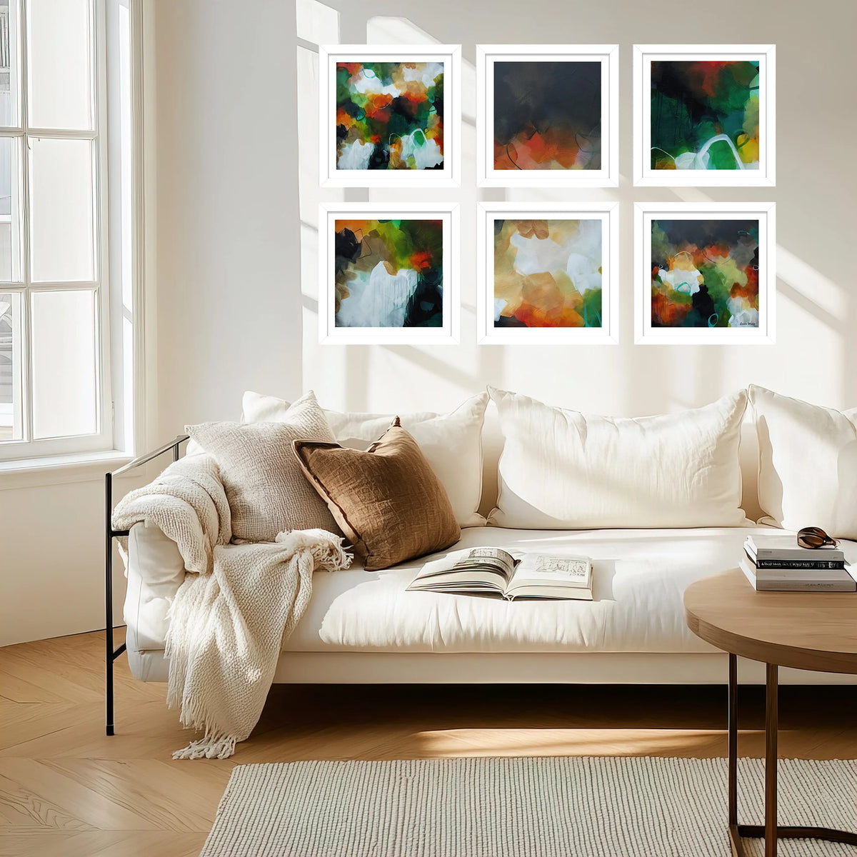 Six framed abstract paintings in a 2x3 grid are displayed on a white wall above a cream-colored sofa in a bright, modern living room.