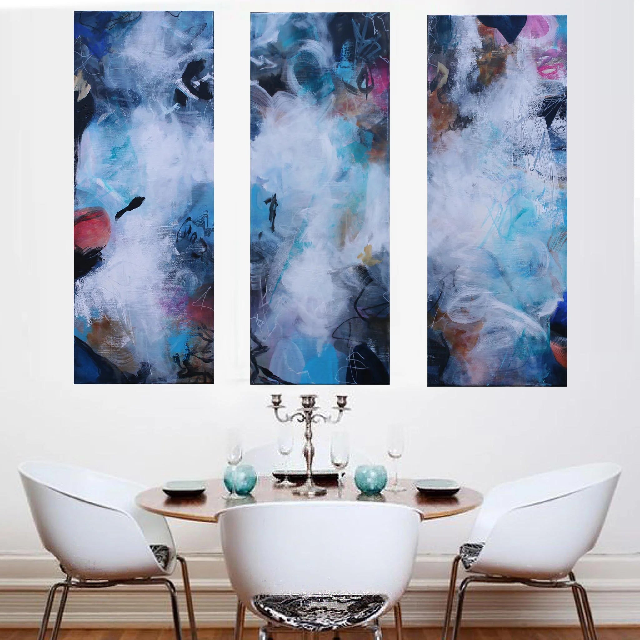 Three abstract wall art pieces above a dining table with chairs.