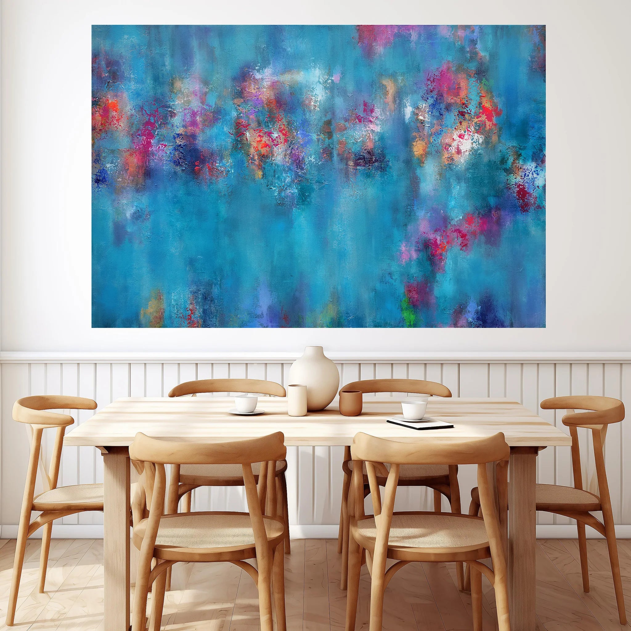 A large abstract canvas wall art print featuring vibrant blue, teal, purple, and pink brushstrokes, displayed in a dining room setting above a light wood table and chairs.