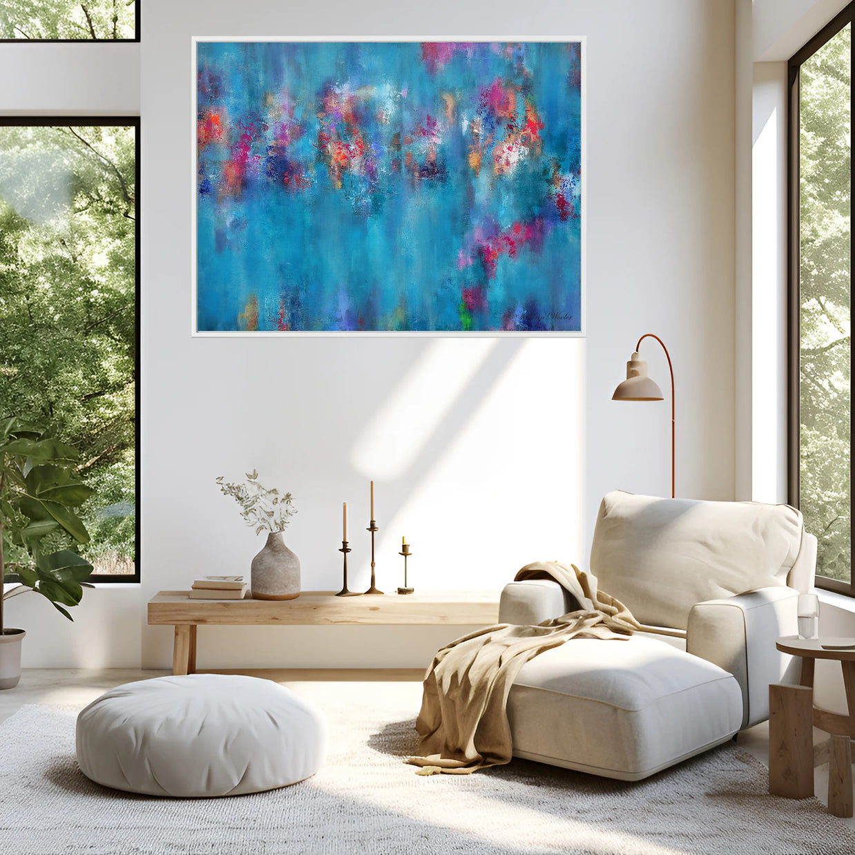 An abstract canvas wall art print featuring vibrant blue, teal, and pink brushstrokes, displayed in a modern living room setting above a beige chaise lounge and ottoman.