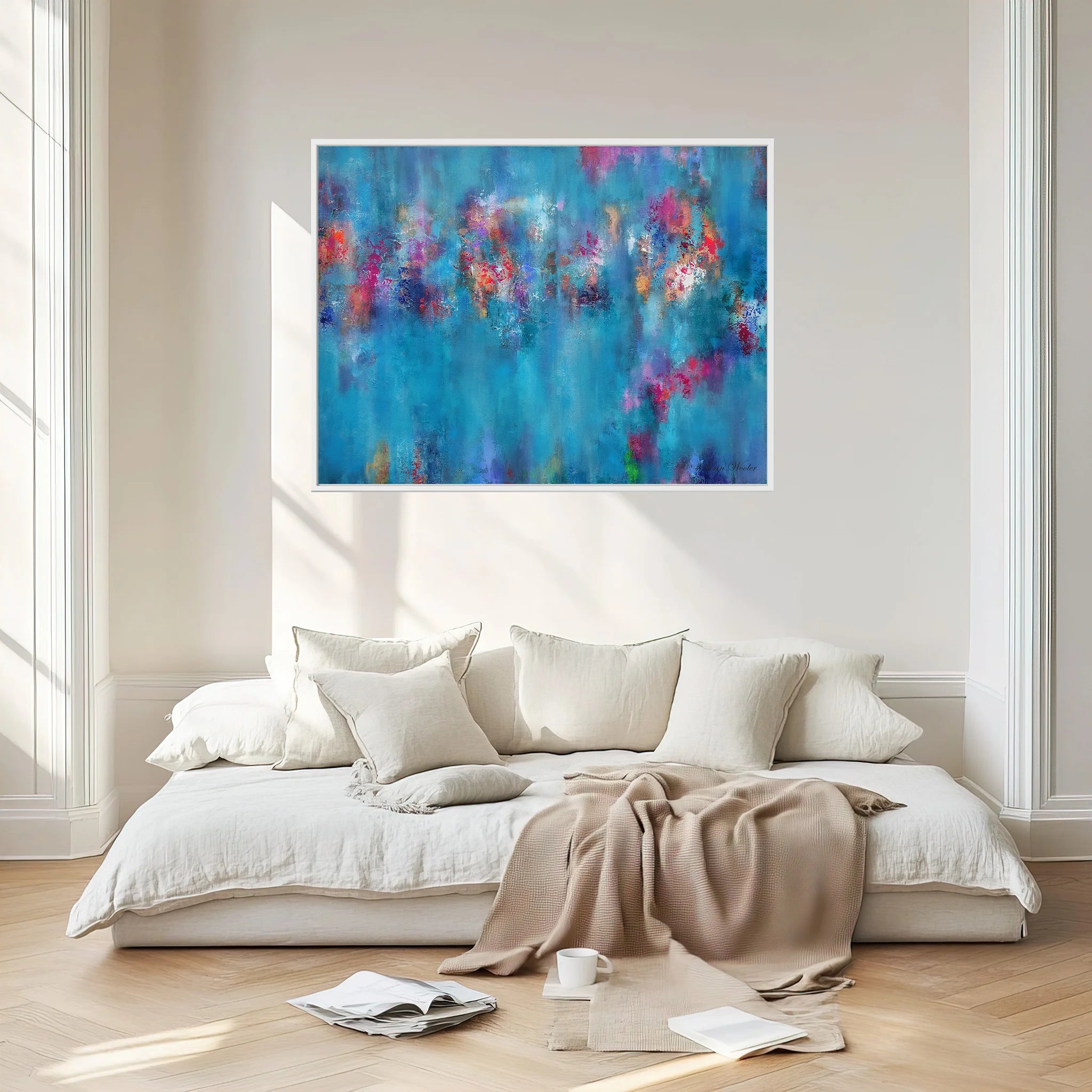 An abstract canvas painting with a vibrant blue background and colorful brushstrokes of pink, purple, orange, and yellow, displayed on a beige wall above a modern white sofa in a bright, modern living room.