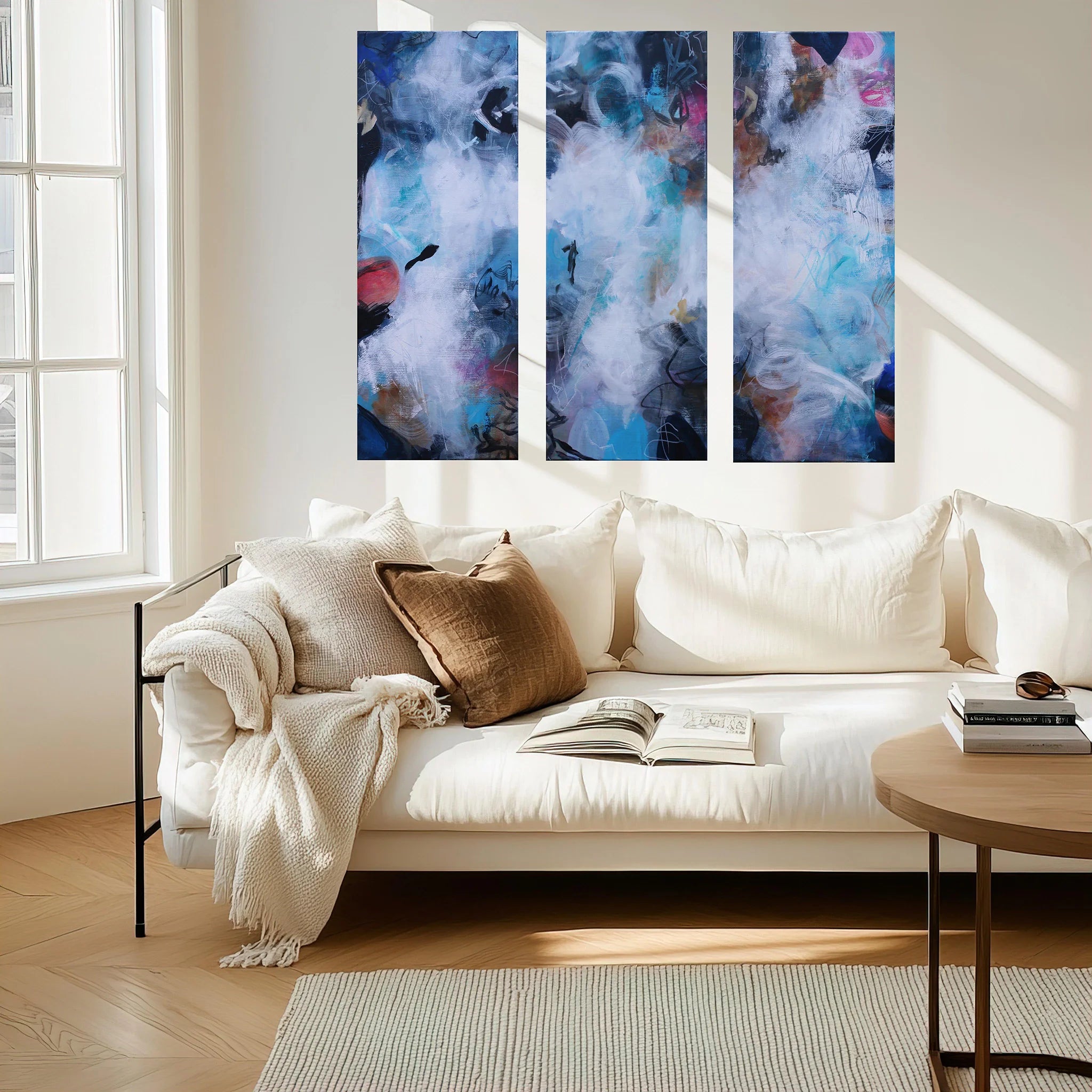 Three abstract paintings above a white sofa in a living room.