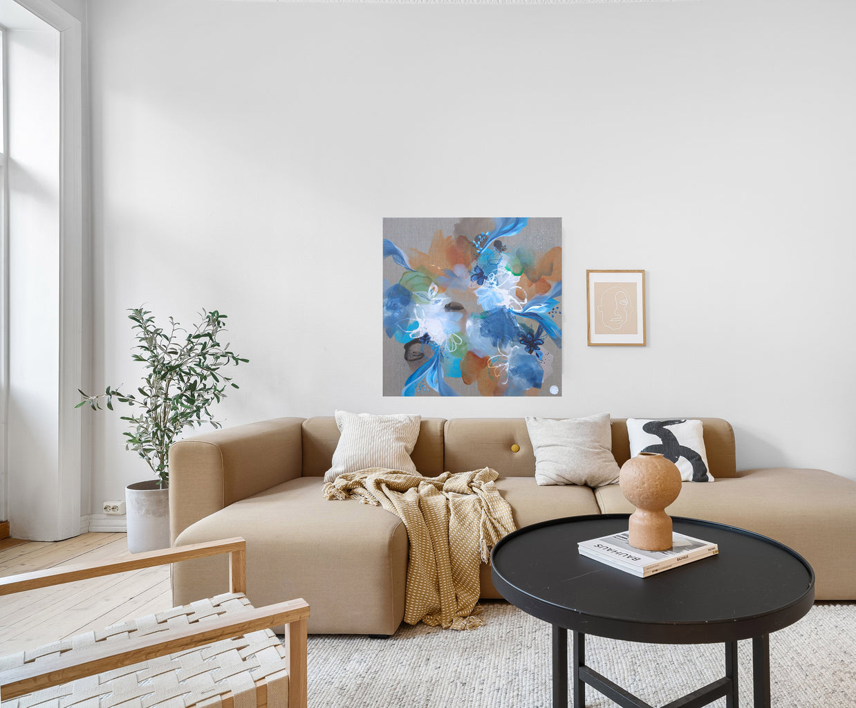 Modern living room with a beige sectional sofa, round black coffee table, and abstract artwork on the wall.