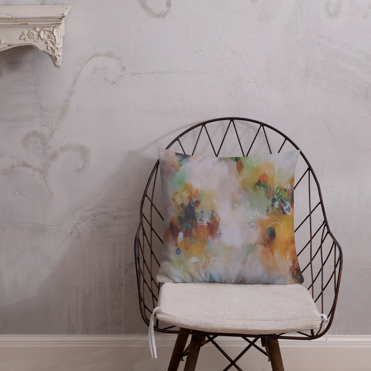 Decorative pillow with a floral pattern on a wire chair against a textured wall.
