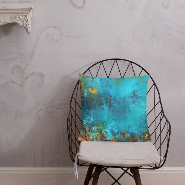 Abstract blue and gold pillow on a black wire chair against a textured wall.