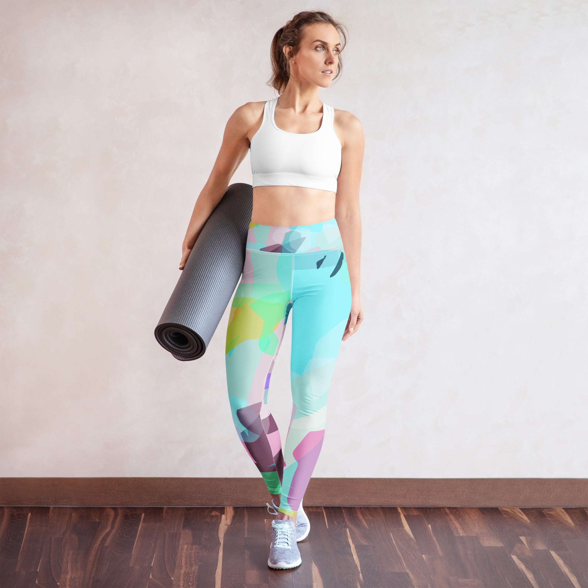 Woman holding a yoga mat wearing colorful leggings and a white sports bra.