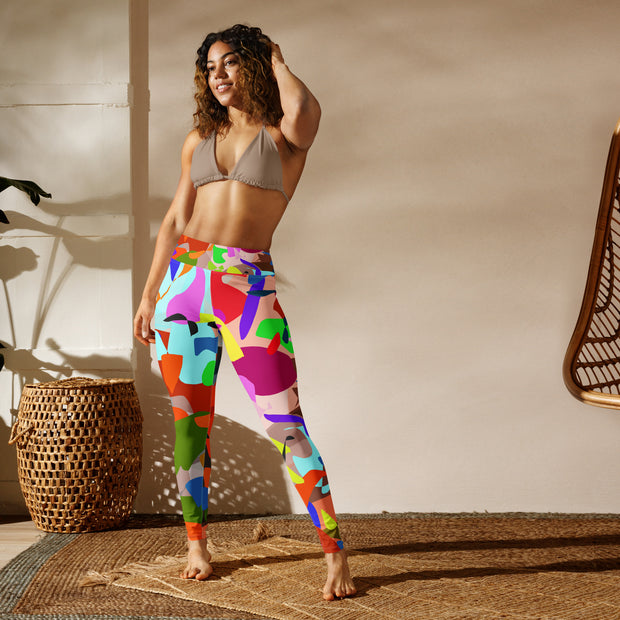 Woman wearing colorful patterned leggings and a gray sports bra standing against a neutral wall.