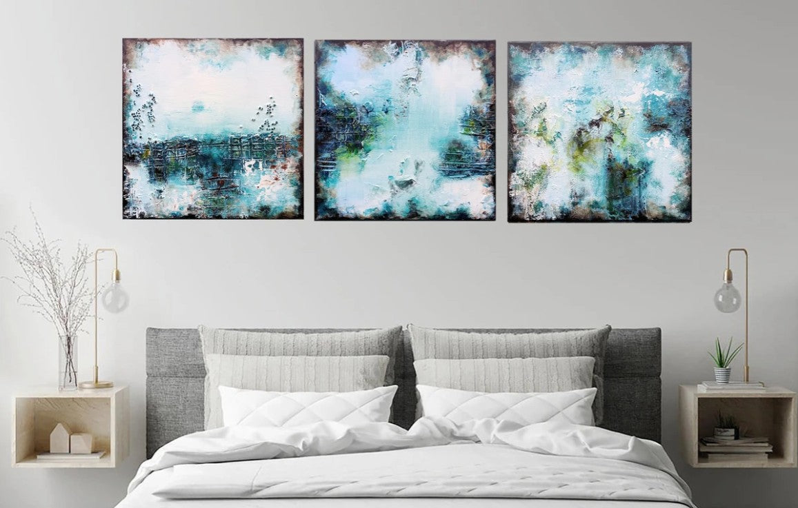 Three abstract paintings above a bed in a bedroom setting.