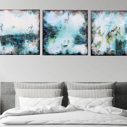 Three abstract paintings above a bed in a bedroom setting.