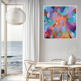 Colourful abstract patinting hanging above light oak dining table and chairs with view through open patio doors of ocean waves