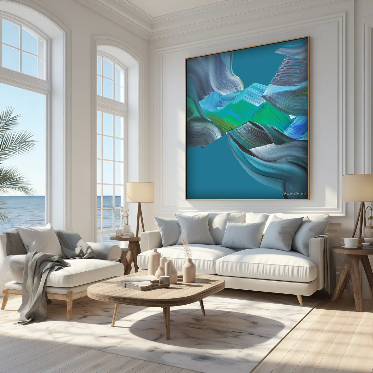 A large framed abstract wall art print hangs above a white sofa in a bright, modern living room. The artwork features flowing blue, teal, gray, and white brushstrokes, while the room has white walls, light wood floors, and natural light coming from tall windows.