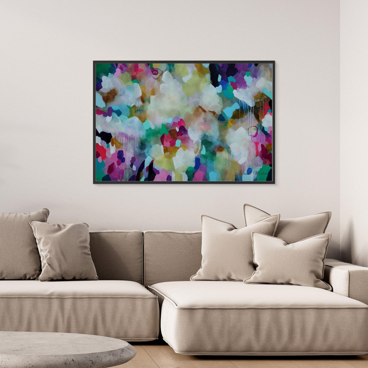 A colorful abstract canvas wall art print with a black frame, hanging on a light beige wall above a modern beige sectional sofa with neutral throw pillows.