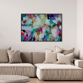 A colorful abstract canvas wall art print with a black frame, hanging on a light beige wall above a modern beige sectional sofa with neutral throw pillows.