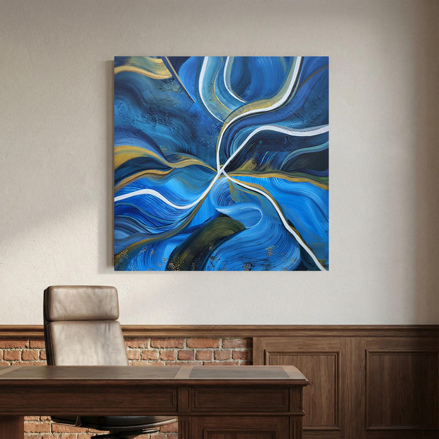 Abstract blue canvas wall art with swirling brushstrokes and white and gold flowing lines, displayed above a wooden desk in a modern office setting with a leather chair and brick wainscoting.