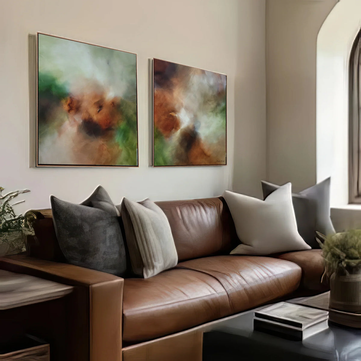 Two framed abstract wall art prints with green, brown, and cream tones hang above a brown leather sofa with gray and cream pillows in a modern living room setting.