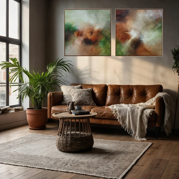 A styled living room featuring a pair of abstract canvas wall art prints hanging above a brown leather sofa. The prints showcase soft, blended abstract patterns in earthy tones of brown, green, and beige.