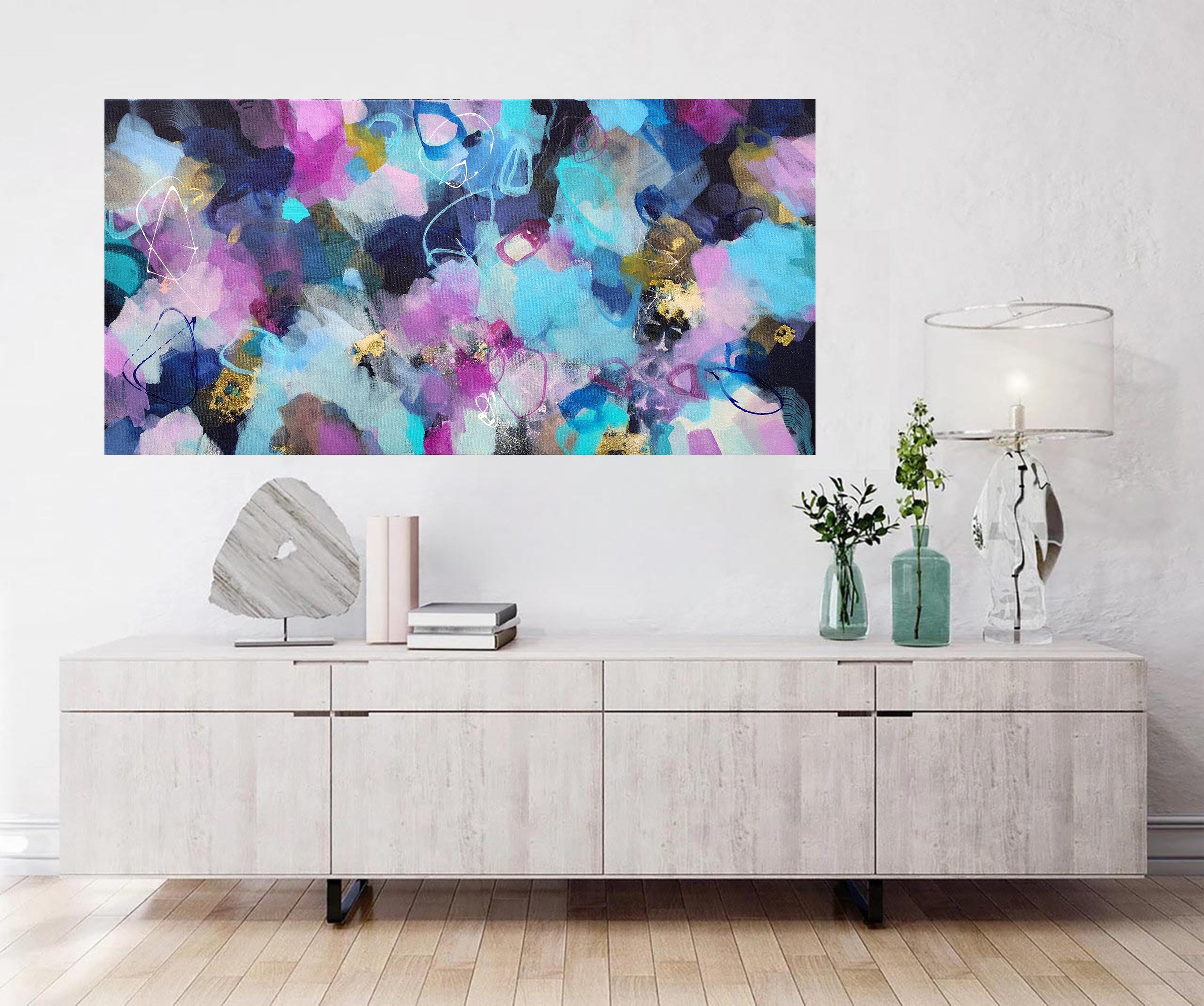 Abstract colorful painting on a wall above a wooden cabinet.