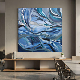 Large square abstract wall art featuring flowing blue, white, and gray brushstrokes, displayed above a wooden console in a modern office or dining room setting.