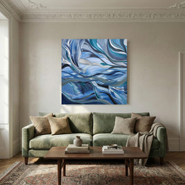An abstract canvas painting with swirling blue, navy, and white patterns hangs on a beige wall above a green sofa in a styled living room.