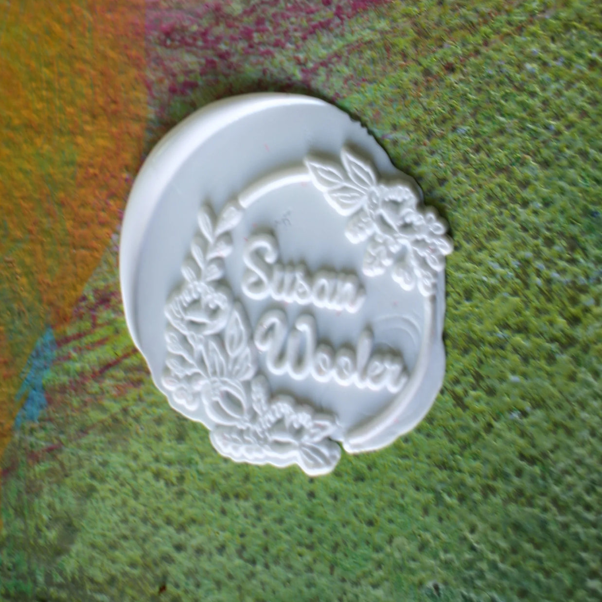 White stamp with 'Susan Wooler' engraved on a textured green surface