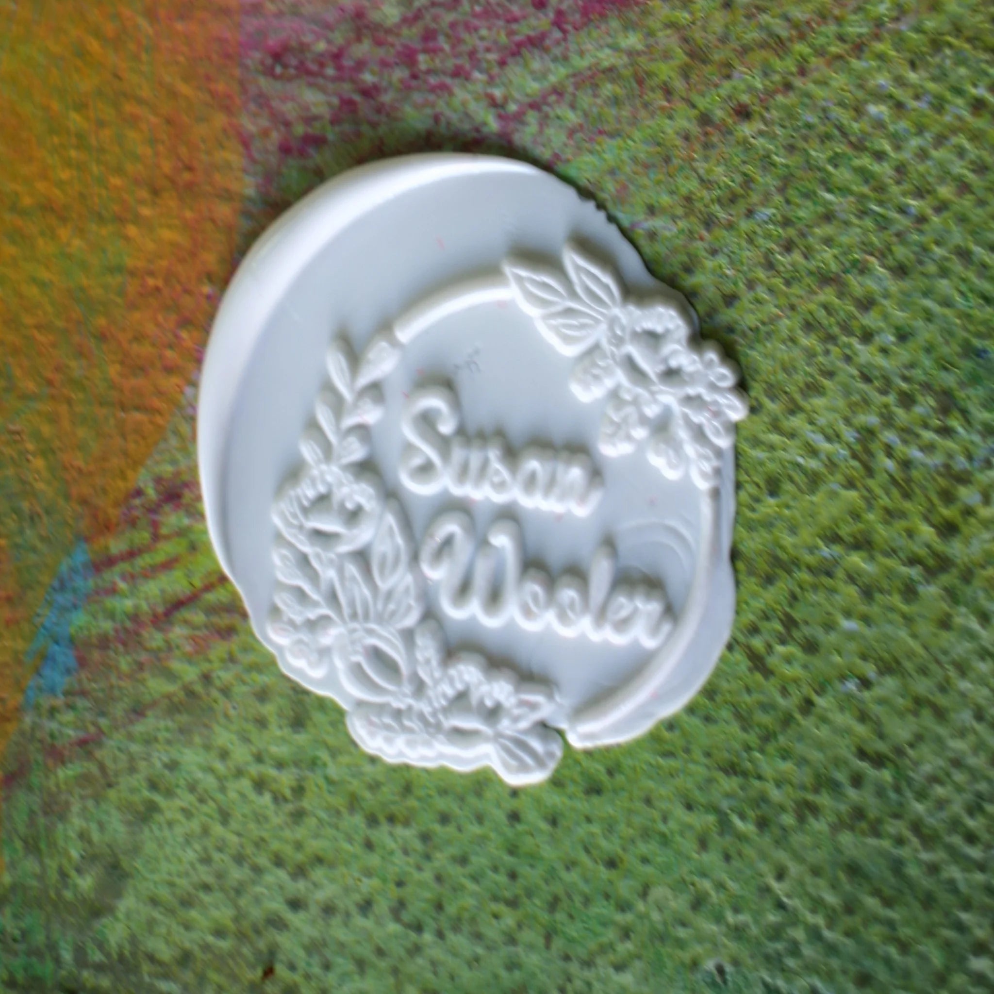 White stamp with 'Susan Wooler' engraved on a textured green surface